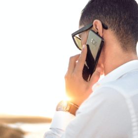 man holding smartphone standing in front of calm body of water